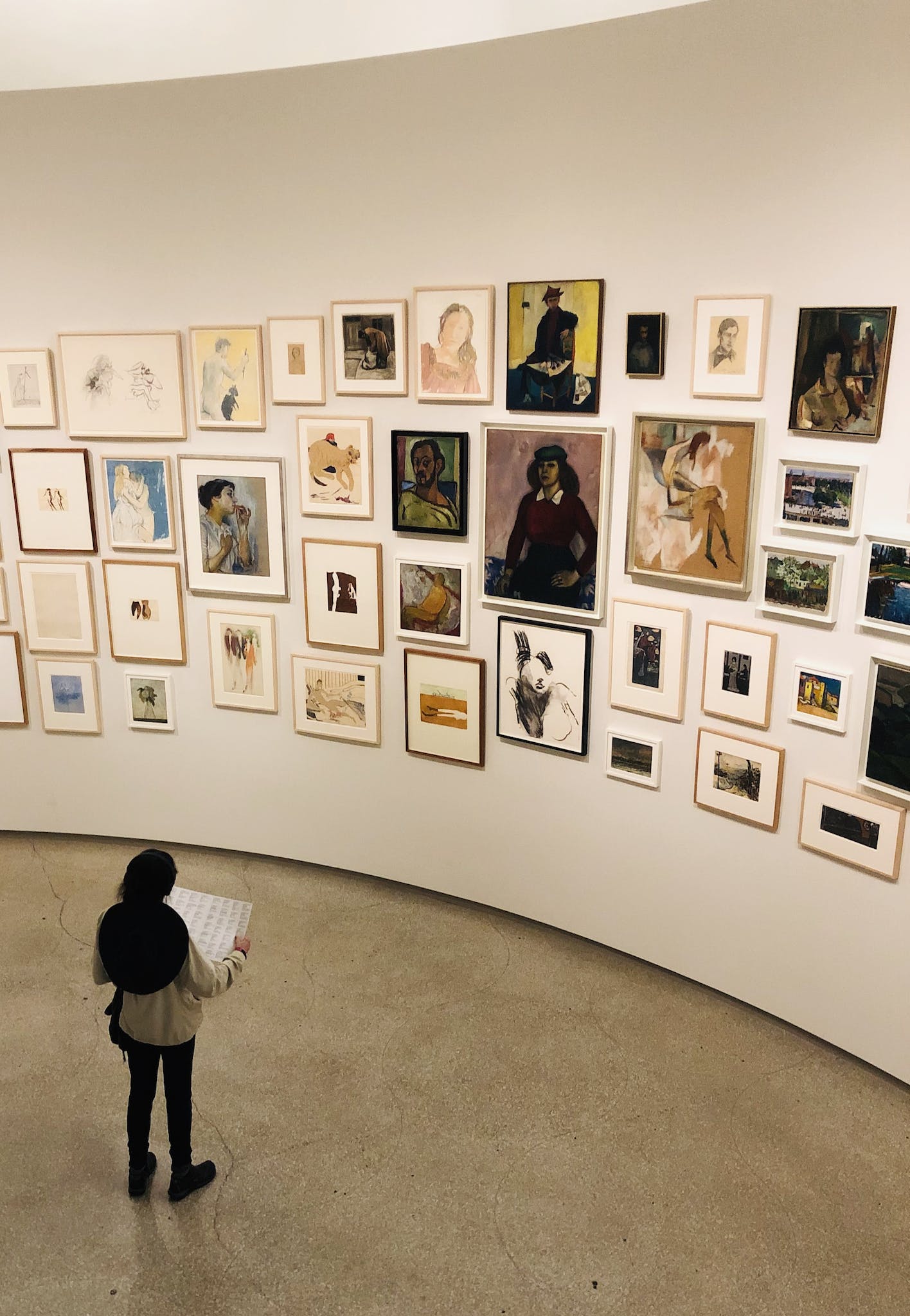 Unrecognizable woman near wall with collection of pictures in gallery